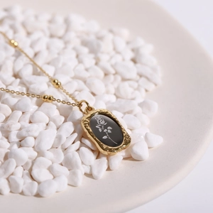 Detail of vintage gold necklace with black rose pendant on white pebbles