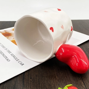 Close-up of white ceramic mug with red heart-shaped handle on a wooden desk surface