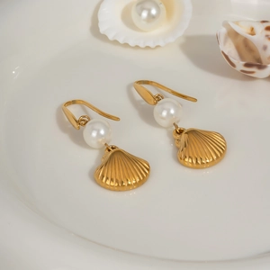 Detail shot of gold shell earrings with white pearl accent on a decorative tray