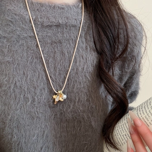 Gros plan du collier avec pendentif cheval doré et perle porté sur un pull en maille douce