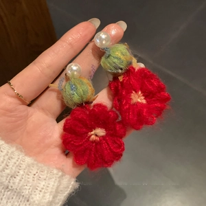 Detail of red knitted flower earrings with white pearls and woven yarn texture