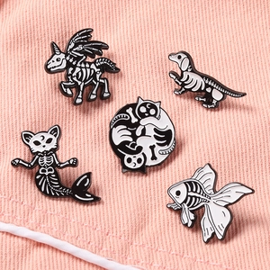 Détail de pins émaillés noir et blanc en forme de crânes d'animaux sur tissu rose