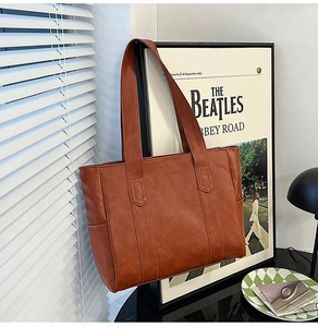 Brown leather tote bag featuring long shoulder straps placed in a cozy vintage setting