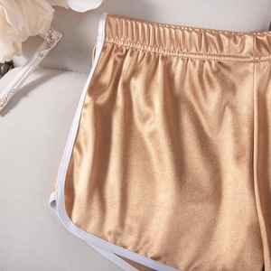 Detail of metallic gold sports shorts featuring white piping and elastic waistband
