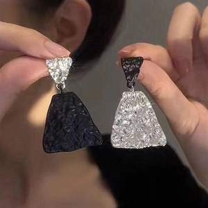 Close-up of asymmetrical geometric earrings with black and silver textured metal surfaces