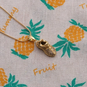 Macro view of gold-plated sneaker pendant with zircon pavé and gold snake chain