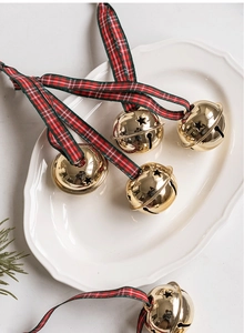 Detail of golden Christmas bell with red and green plaid ribbon on white plate