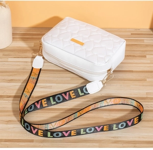 Close-up of white heart-quilted crossbody camera bag with colorful LOVE strap on wood