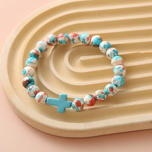 Close-up of beaded bracelet with blue, orange, white stones and a blue cross pendant