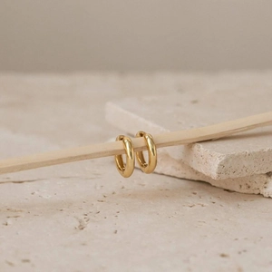 Macro shot of gold hoop earrings on a wooden display with a minimalist stone background