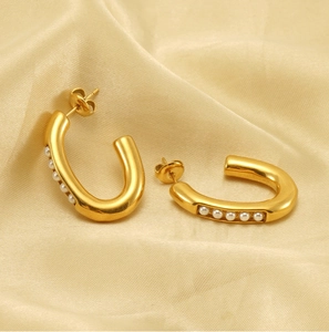 Close-up of gold U-shaped earrings with pearls on soft champagne satin background