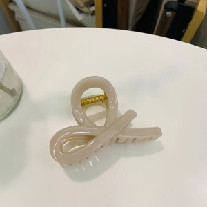 Cream colored resin claw clip with gold spring shown from a top-down minimalist view