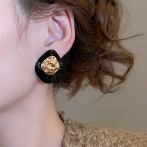 Retro black resin earrings with hammered gold center worn by model in warm lighting