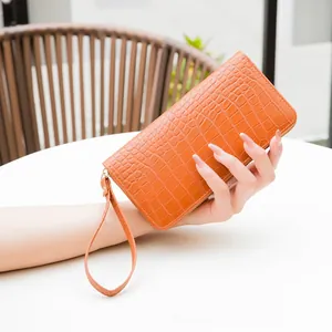 Detail of orange embossed crocodile pattern long wallet with wrist strap held by hand