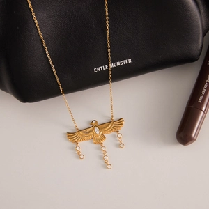 Collar con colgante de águila en acero de titanio dorado y circón en fondo cálido