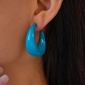 Close-up of a vibrant blue acrylic C-shaped hoop earring worn by a model