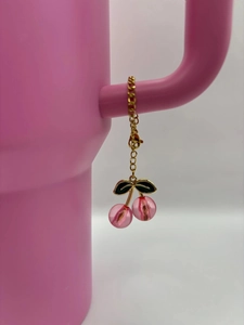 Pink cherry charm keychain hanging on a cup handle with gold chain and leaf details