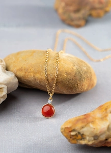 Detail of a round red gemstone pendant with a gold chain and small zircon accent