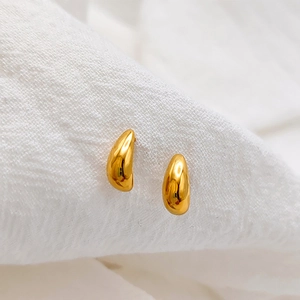 Vista macro degli orecchini a goccia in oro 18K lucido su tessuto a pieghe bianco
