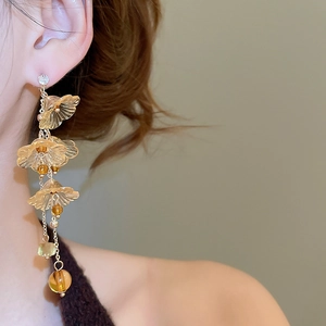 Macro shot of elegant amber resin flower drop earrings with golden tassels on a model