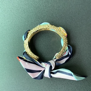 Close-up of matte gold bangle with blue and pink striped silk scarf ribbon detail