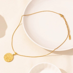 Macro detail of 18k gold plated hollow round coin pendant on a sleek porcelain surface