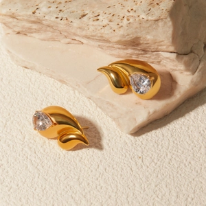Golden stainless steel wing earrings with clear zircon stones on natural stone background