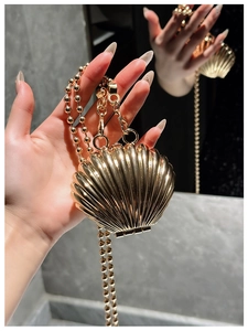 Detail of a mini gold shell-shaped bag with a beaded metal chain and metallic finish