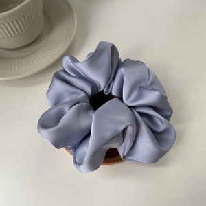 Close-up of soft lilac satin scrunchie with silky pleated texture on a wooden tray