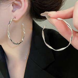 Detail of silver twisted hoop earrings featuring polished metallic texture and wave pattern