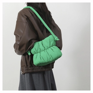 Green puffy quilted shoulder bag with knotted strap detail shown on a model's shoulder