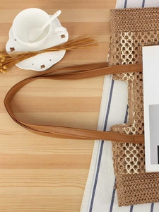 Modische khakifarbene Strohtasche mit braunen PU-Riemen auf einem Holztisch