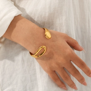Close-up of golden asymmetric open cuff bracelet with organic curves on white fabric
