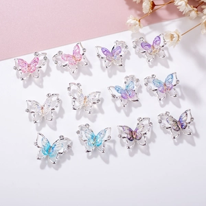 Mix of 11 laser aurora butterfly nail charms with pearls and rhinestones on pastel background
