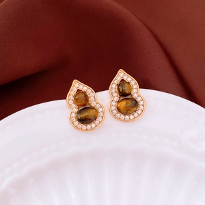 Gros plan de boucles d'oreilles en or rose avec pierres oeil de tigre et détails zircon