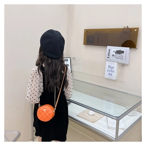 Detail of orange quilted round crossbody bag with gold flower logo on a child model