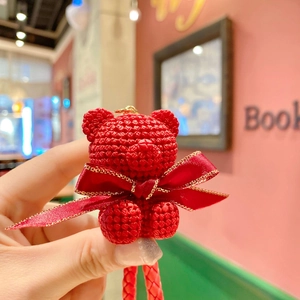 Close-up of red hand-woven sitting bear keychain with gold-edged ribbon and knit texture