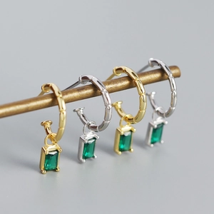 Macro detail of bamboo-textured C-shape earrings with green emerald zircon pendants