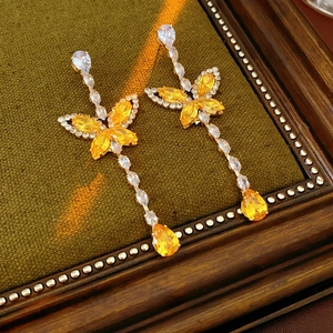 Macro detail of butterfly drop earrings with yellow zircon on green velvet background