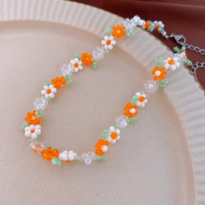 Close-up of handmade orange and white beaded flower necklace with green leaf accents