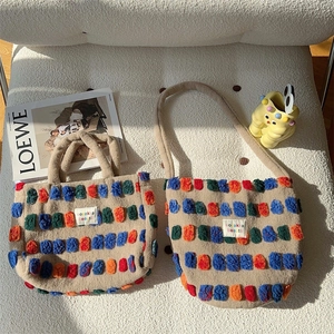 Detail of plush bucket bags with colorful pom-poms and embroidered logo on white surface