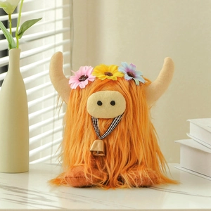 Orange highland cow plush toy with flower crown and golden bell on marble surface
