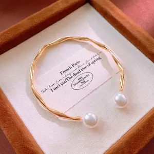 Elegant gold wavy open bangle featuring two white pearls on a brown velvet jewelry box