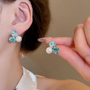 Detailed close-up of blue crystal and pearl stud earrings worn on ear for texture