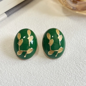 Close-up of vintage oval enamel earrings with golden leaf patterns on textured surface