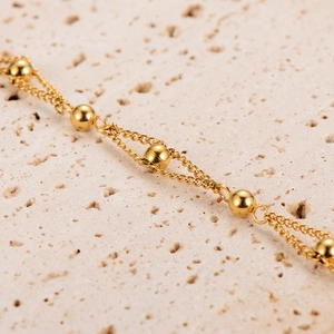 Double-layered gold bead bracelet in polished stainless steel on a textured stone surface