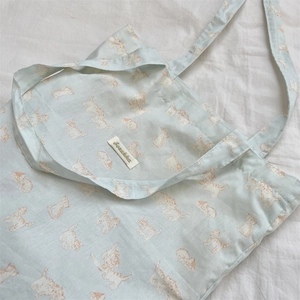 Detail of mint green canvas tote bag with orange cartoon cat print and woven label