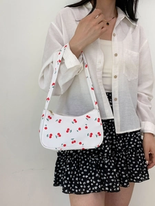 Detail of white nylon underarm bag featuring vibrant red cherry patterns and shoulder strap