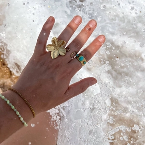 Bagues fleur dorées et bracelets en perles de style bohème sur fond de vagues de mer