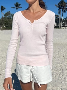 Detail of pink V-neck ribbed long sleeve shirt with button placket in a beach setting